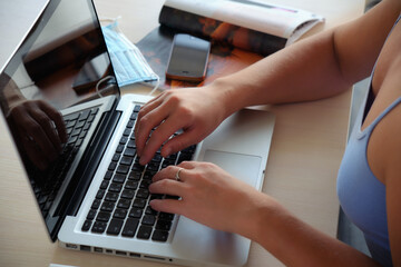 Fototapeta na wymiar girl prints text on a laptop, next to a magazine and a medical mask