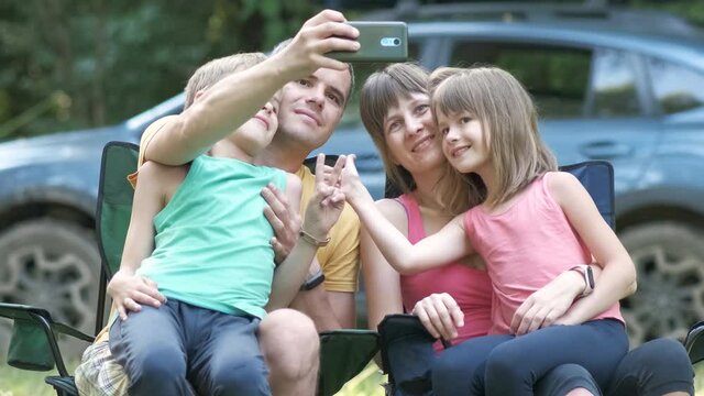 Happy young family sitting together at campsite and taking selfie with mobile phone.