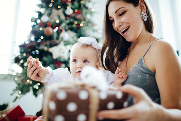 Mother and daughter open New Year's gifts under the Christmas tree. 