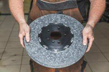 mechanic in a dirty clothes holds a carbon brake disc