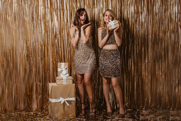 Pretty girls enthusiastically look into camera and hold beautiful boxes with gifts on brilliant...