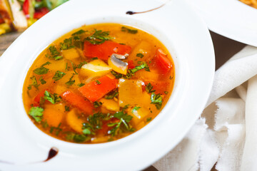 Traditional vegetable soup broth in a white plate on a table in a restaurant.