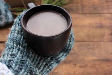 Woman hands in mittens holding cup of hot chocolate or cocoa with milk on vintage table background. View from above. Flat lay style. Copy space