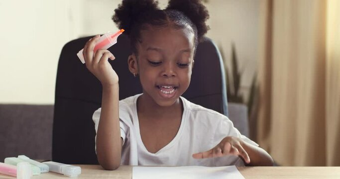 Funny cute dark-skinned preschool girl african american lady child speaks emotionally, happy facial expression, mixed race toddler actively moves gesticulates hands shows drawing, view from web camera