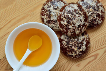 Honey in a white cup and chocolate gingerbread on a wooden background