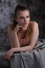 Fototapeta premium Portrait of a beautiful girl in a pink blouse on gray sheets