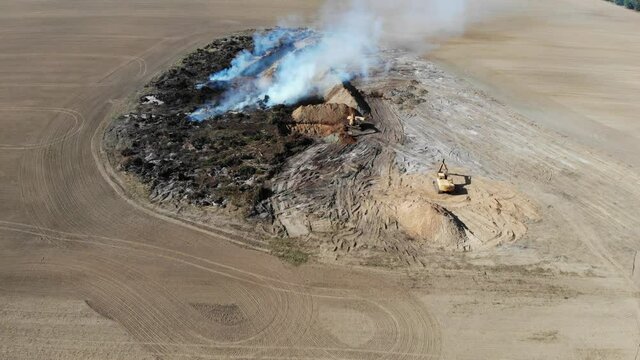 Excavators clear the field from the forest to increase farmland. Burning trees in a pit after increasing the plowed field. Inefficient farming. Environmental problem. Aerial view 4k.