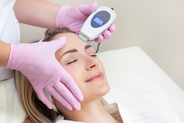 Cosmetologist makes an ultrasonic cleaning of the face of a young woman. close up