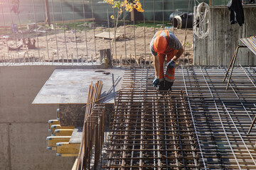 workers using steel wire and pincers to secure rebar before concrete is poured over it.