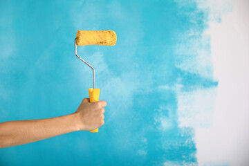 close up of female hand holding paint yellow roller over blue background-repair, construction and building tools concept. Convenient and versatile tool for painting walls.