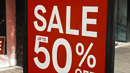 Red sign hanging on a glass window with the inscription sale up to 50% off