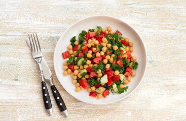 Healthy vegan salad with chickpeas, tomatoes, cucumbers, bell peppers and kale on light wooden background, flat lay