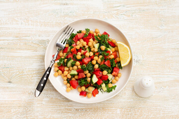 Healthy vegan salad with chickpeas, tomatoes, cucumbers, bell peppers and kale on light wooden background, flat lay