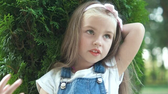 Portrait of pretty child girl standing outdoors in summer park smiling happily.