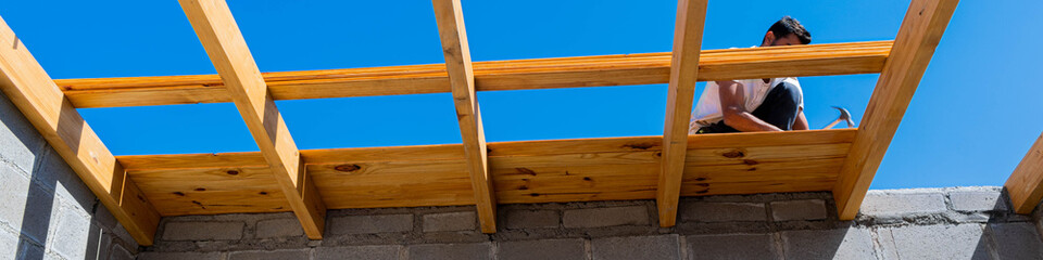 construccion de techo de madera con madera de machimbre colocada con clavos de pulgada y media con hermoso cielo azul y vigas de madera cuadradas