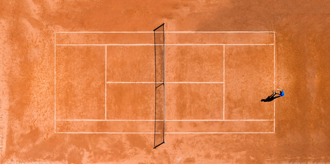 Aerial view of a person playing tennis on a clay court during theCovid-19 outbreak. A clay court is...