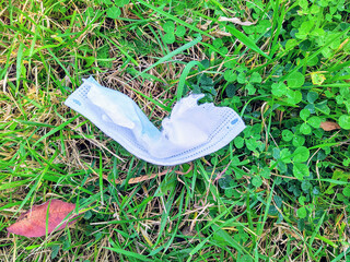 Environmental pollution with medical masks during the COVID19 coronavirus pandemic. Disposable medical mask garbage lies on the green grass in spring. Used infected trash is thrown into environment.
