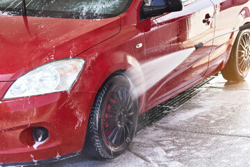 Front light of red car washed in self serve carwash, liquid reflected on side door, high pressure...