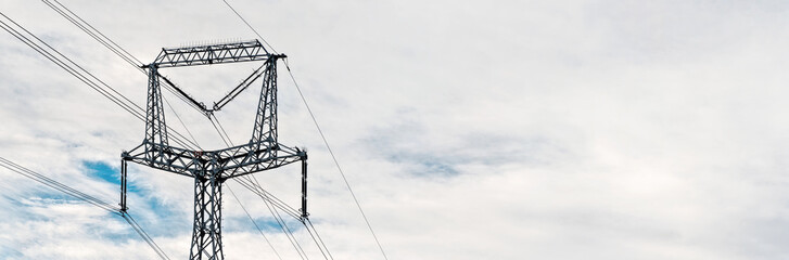 Looking up steel power pylon construction with high voltage cables against cloudy sky. Wide banner for electric energy industry with space for text on right side