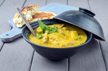 Traditional Indian fish curry with pita bread offered as close-up in a design in bowl