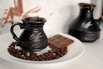 Roasted coffee beans and chocolate, lying on a plate, next to a mug of coffee and cezve