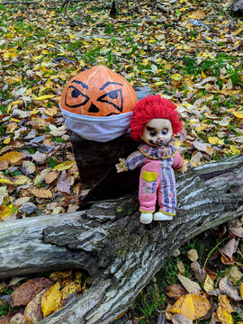 Halloween pumpkin in a disposable mask with a clown doll on a background of autumn leaves