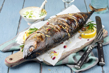 Traditional Australian barbecue bonito fisch with tzatziki and lemon slices offered as closeup on a rustic wooden board