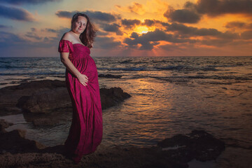 Fototapeta premium pregnant woman by the sea at sunset in a beautiful dress
