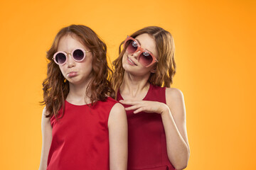 Happy sisters in red dresses on a yellow background are having fun and gesticulating Copy Space