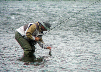 Adult man is fishing and holding the fish with his hands in the lake.