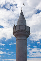 The seagull is flying over the minaret on a cloudy day. Mosque is the holy place for the muslims to pray.