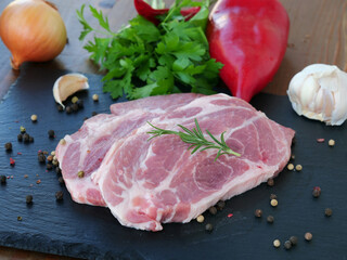 Raw pork neck boneless collar slices over slate platter with vegetables