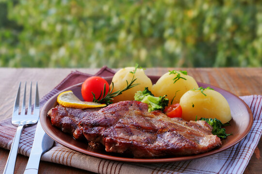 Juicy pork steak with boiled potatoes and rosemary on plate over an outdoor table