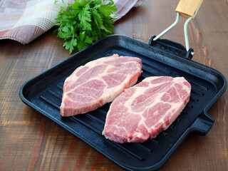 Two slices of raw pork neck fat slabs in a square cast iron grill pan on wooden table