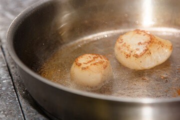 The chef is frying scallops in oil in a frying pan