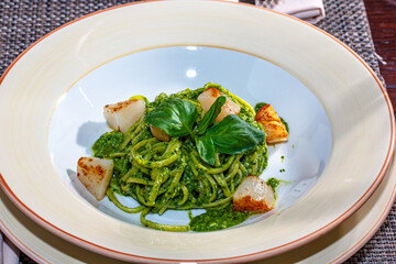 Pasta (spaghetti) with pesto sauce and scallops is on the plate.