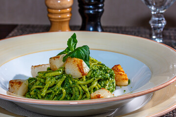 Pasta (spaghetti) with pesto sauce and scallops is on the plate.