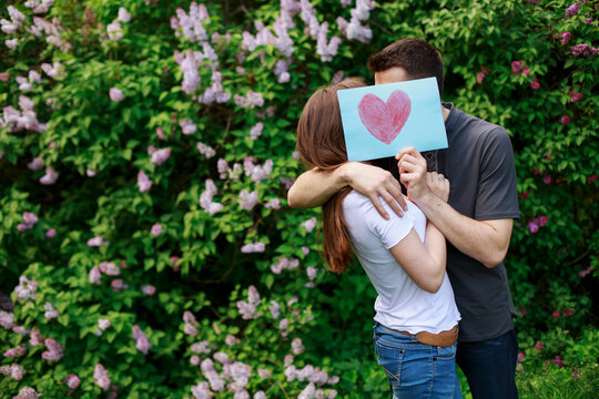 Loving Young Couple hold a card with a heart outdoors. love story concept. heart in man and woman hands. romantic date in nature. romantic moment in background