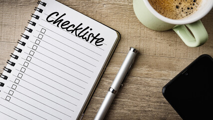 Checkliste. Flat Lay. Arbeitsbereich mit Notizblock, Kugelschreiber, Handy und einer Tasse Kaffee.