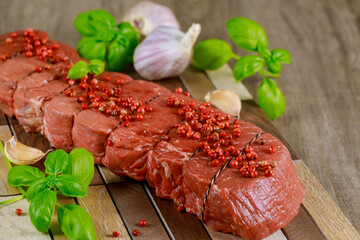 Raw beef steak with garlic and basil on wooden board.