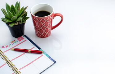 Day planner with a cup of coffee, mask and hand sanitizer on a white top table awaits a session of goal setting.