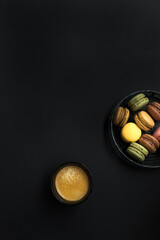 Overhead view of a foamy coffee next to a metal circled tray full of french macaroons.