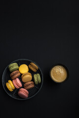 Horizontal and vertical homemade macaroons inside a circled wire tray next to a coffee cup on a black background.