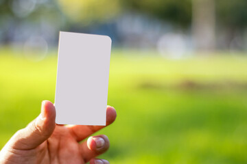 Hand holding a blank card isolated with clipping path, on unfocused background of a green area of ​​a park.