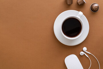 Flat lay with coffee cup, coffee capsules and white earphones on brown background. Copy space.