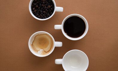 Flat lay with 4 coffee cups, full and empty cups on brown background. Copy space.
