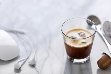 Iced espresso in a glass on a kitchen table, earphones, spoon, copy space.
