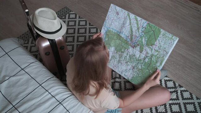 Open Borders, Pack Things, Happy Vacation, Booking Hotel. Woman Traveler Sits On The Floor Near The Bed And Holds A Paper Map In Her Hands