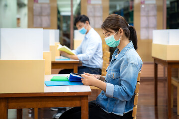 Two Asian university students wearing face mask and sitting in library social distance from other 6 feets to avoid the spread of coronavirus in University.