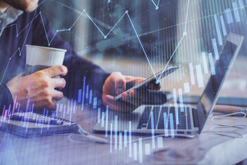 Double exposure of man's hands holding and using a phone and financial graph drawing. Analysis concept.